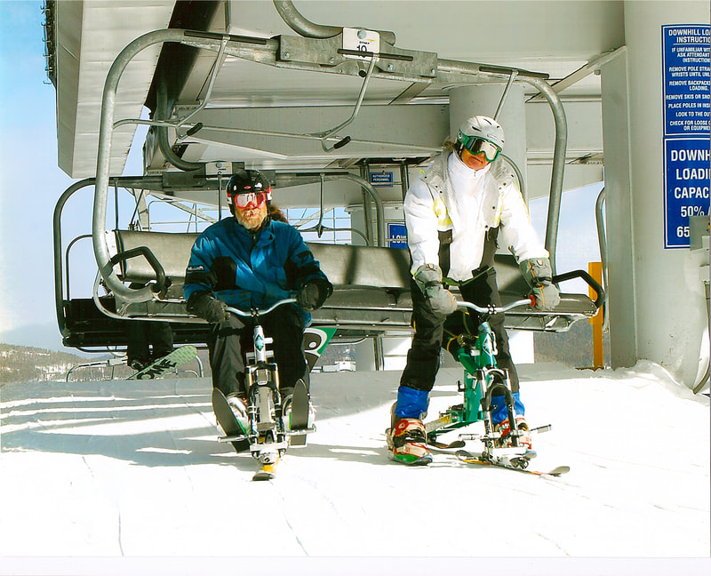 Two ski bikers, one seated and one standing, unloading their iSkibikes from a Breckenridge ski resort chairlift, Breckenridge, Colorado.