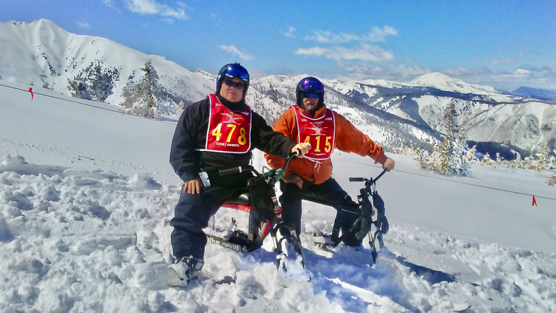 Two adaptive skiers, enjoying renewed skiing agility and freedom on their iSkibikes, pose with the Colorado Rockies in the background, at the National Disabled Veterans Winter Sports Clinic, Snowmass, Colorado.