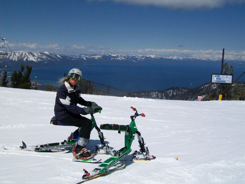At the top of the Heavenly Mountain Resort, with the Sierra Nevada Mountains and Lake Tahoe in the background, ready for skiing action, an adaptive ski biker  poses with two iSkibikes, near South Lake Tahoe, California.